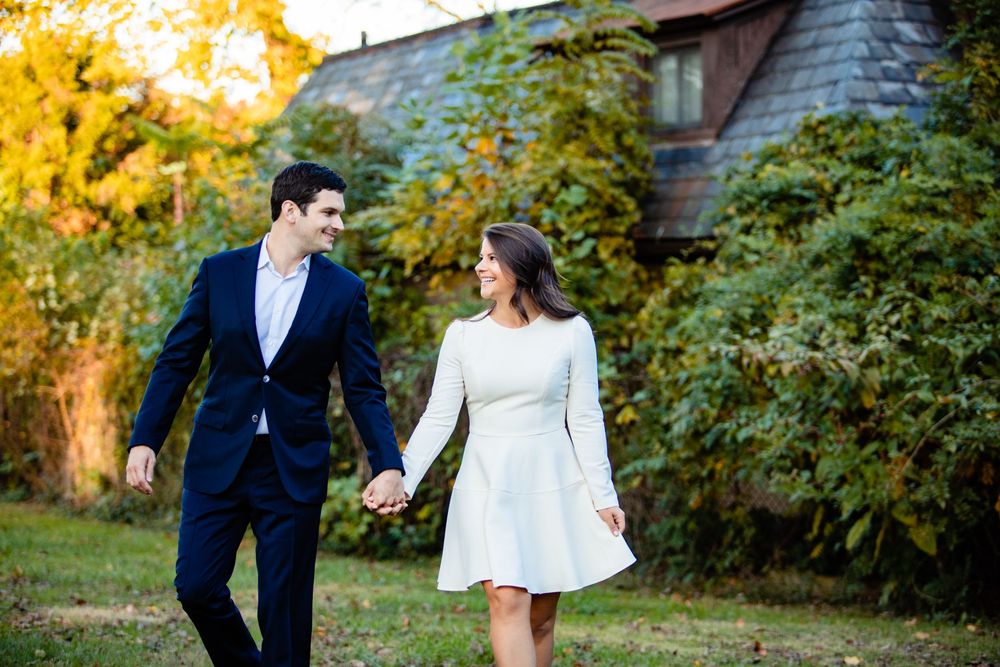 Couple holding hands and strolling through a garden with autumn foliage, woman in a white dress.