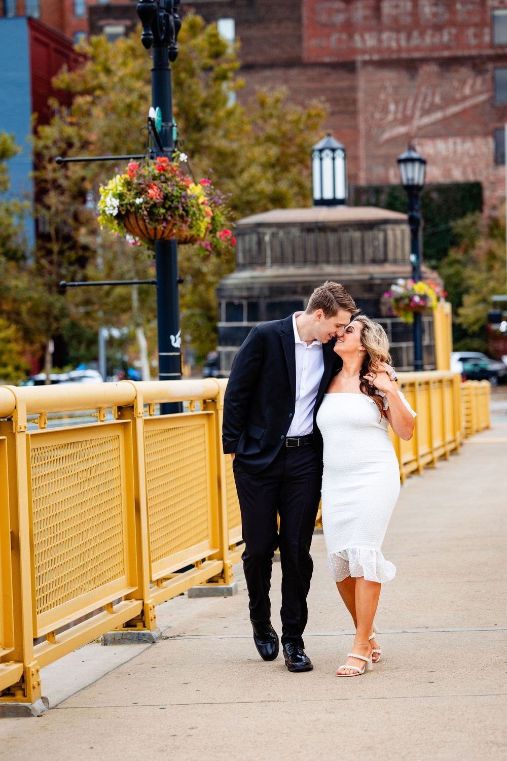 Couple walking closely together on a yellow bridge in an urban neighborhood setting.