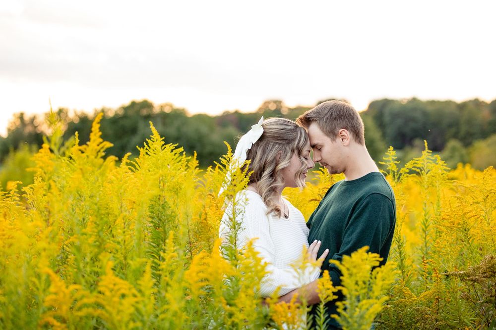 Couple standing face to face in a golden wildflower field at sunset, sharing a tender romantic moment.