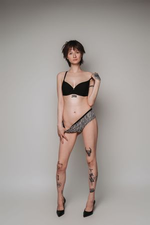 A figure in black lingerie and zebra print shorts poses against a light gray studio backdrop.