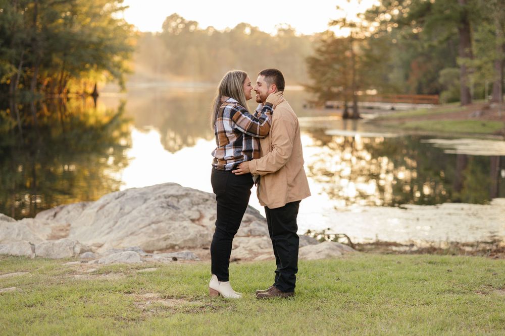 Couple enjoying a tender moment on grassy shore with lake reflections in background.