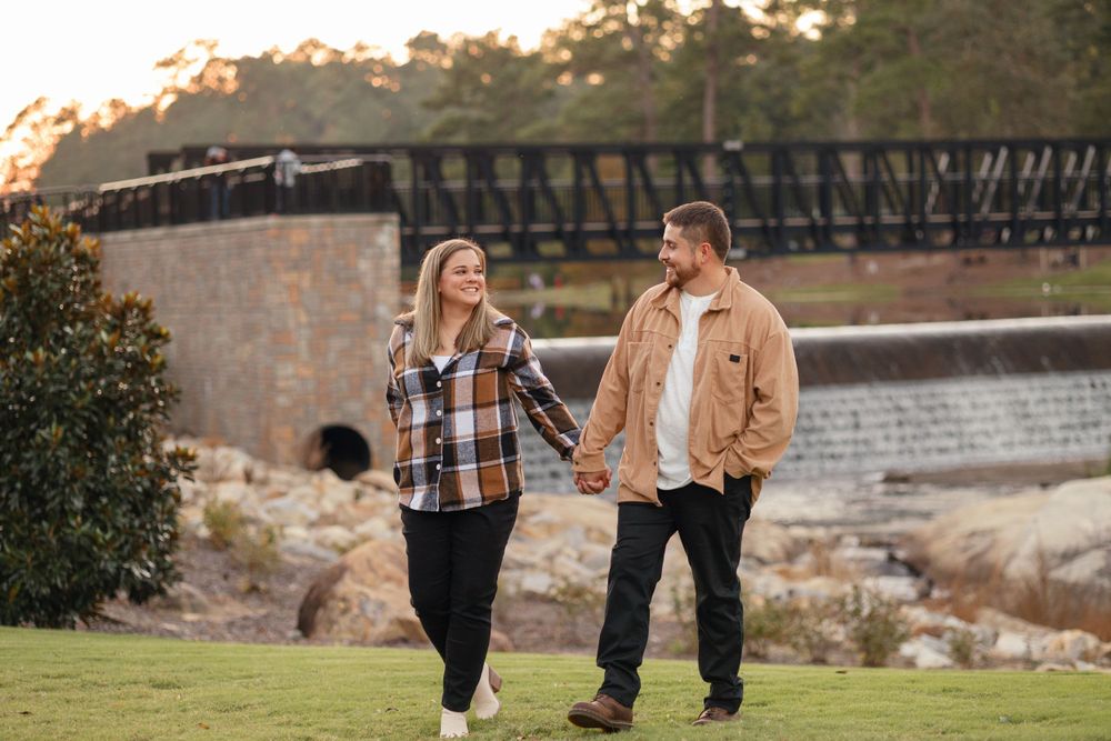 Couple walking and laughing together near stone bridge during sunset.