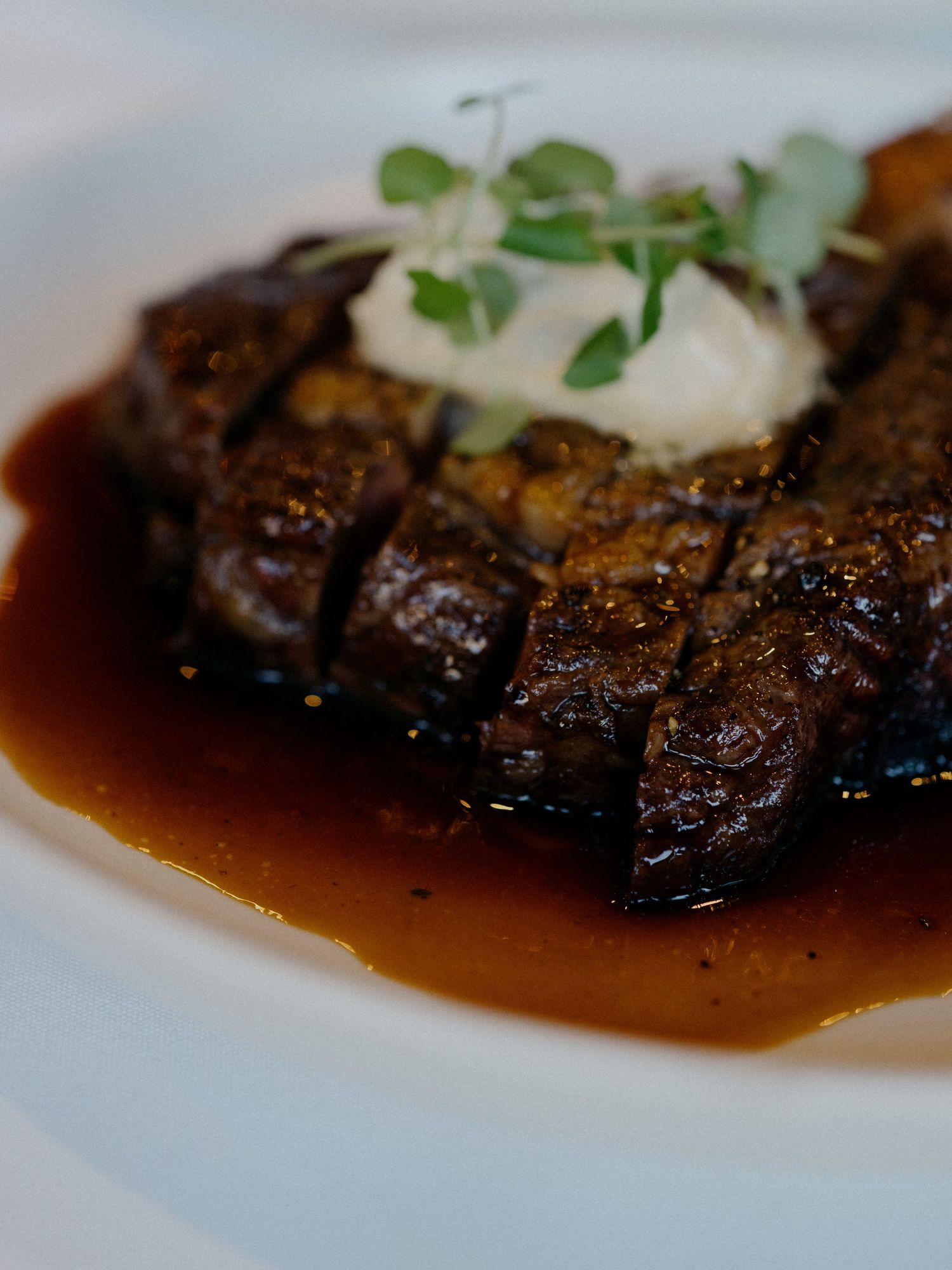 Perfectly cooked steak with garnish and sauce plated elegantly on white dish.