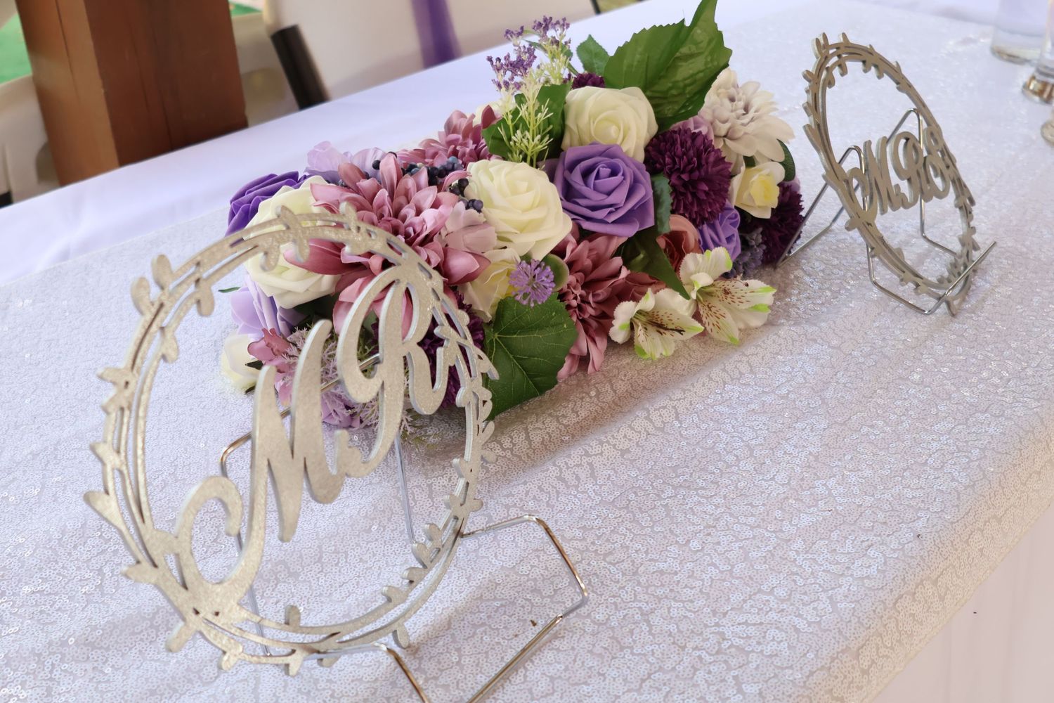 Elegant floral table centerpiece with purple and white flowers on a textured tablecloth.