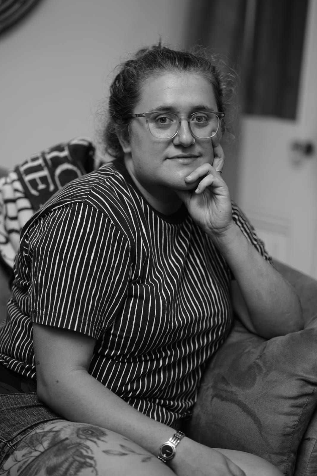 Black and white portrait of a person in a striped shirt sitting on a couch with a contemplative expression.