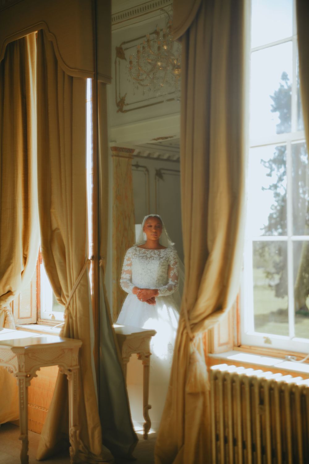 Sunlight streams through tall windows with golden curtains in an ornate room with white crown molding and architectural details.