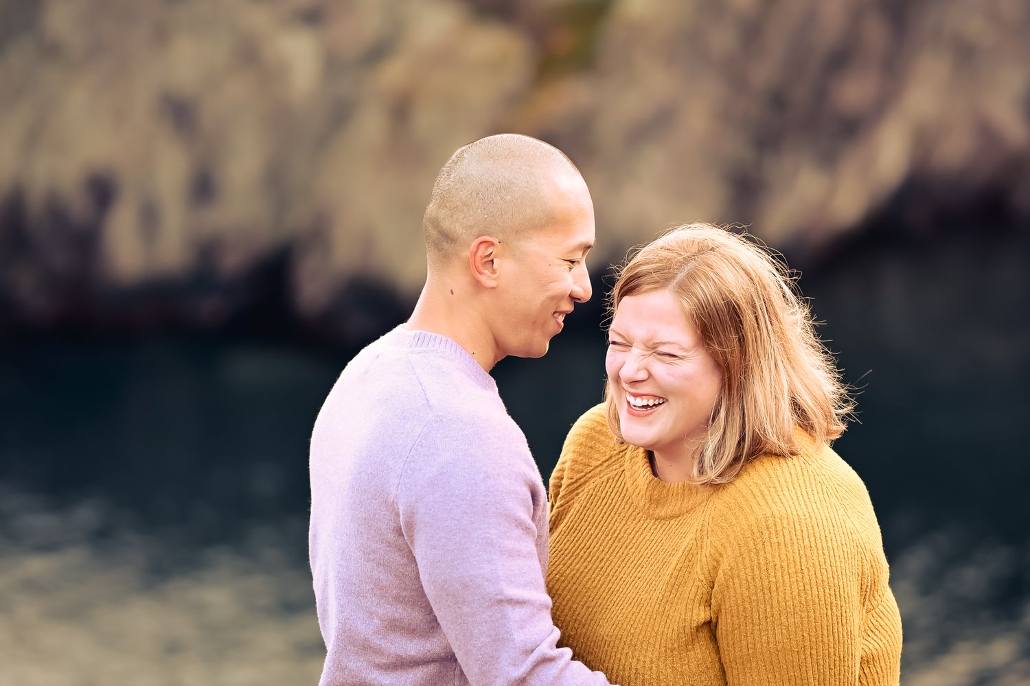 A laughing couple on a rocky shore at sunset, sharing a moment of love in St. John's, Newfoundland.