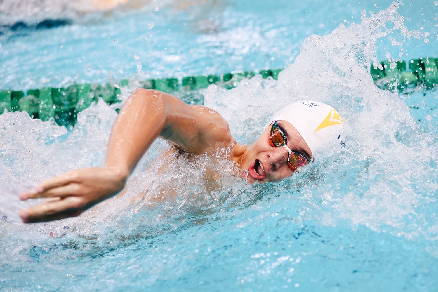 Competitive swimmer performing freestyle stroke in pool with water splashing.