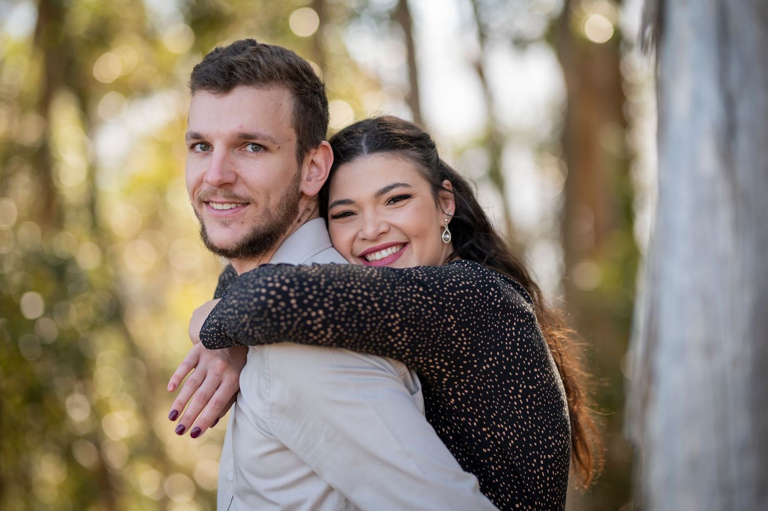 Couple embraces while surrounded by tall trees in an outdoor forest setting during a photoshoot.