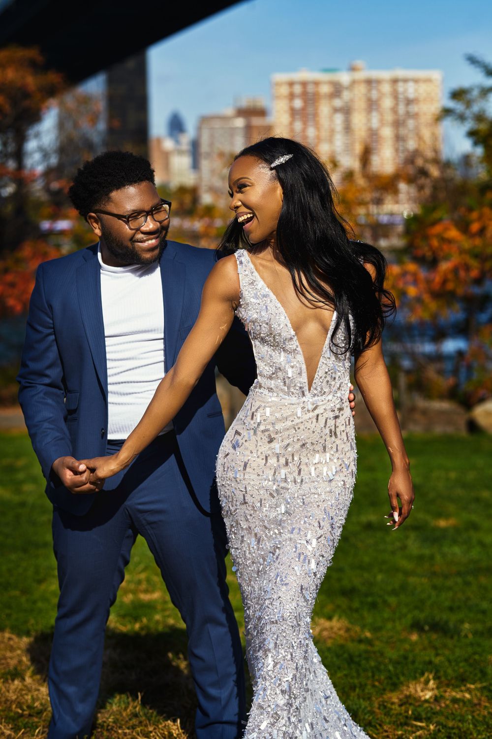Elegant couple in formal attire share a joyful moment together in an autumn park setting with fall foliage at Brooklyn Bridge