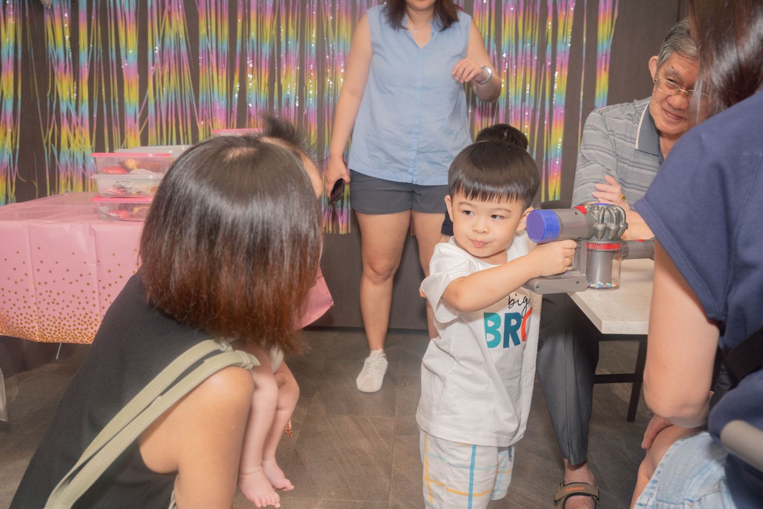 Indoor celebration scene with multiple people standing around in a casual setting with decorative elements.