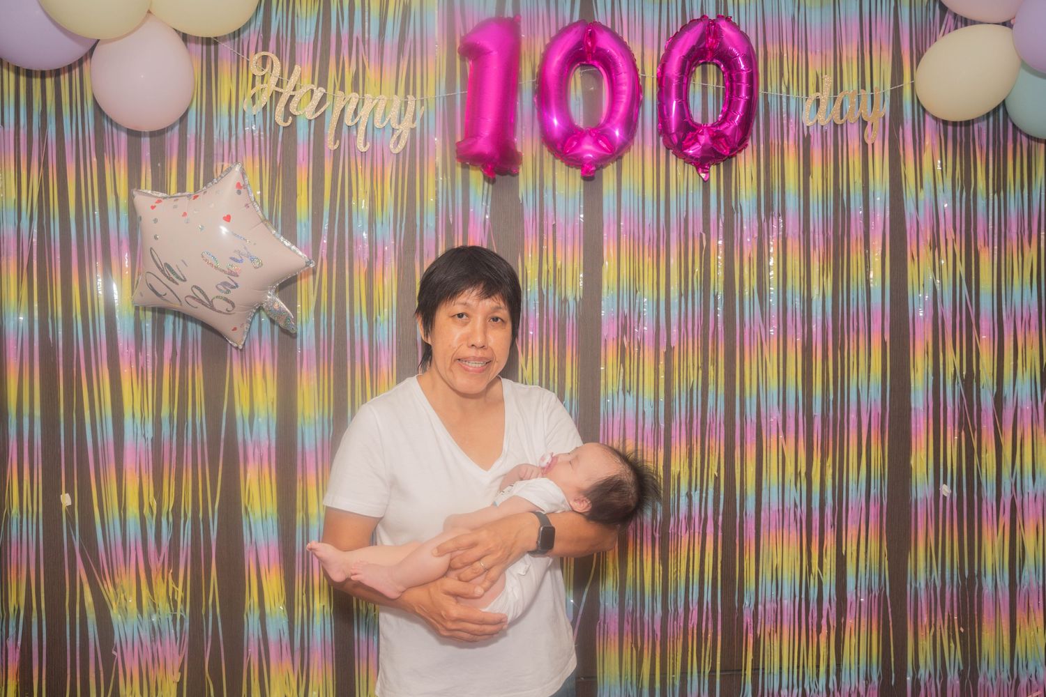 Guests at a 100th birthday celebration pose against a backdrop of pink balloons and colorful streamers.