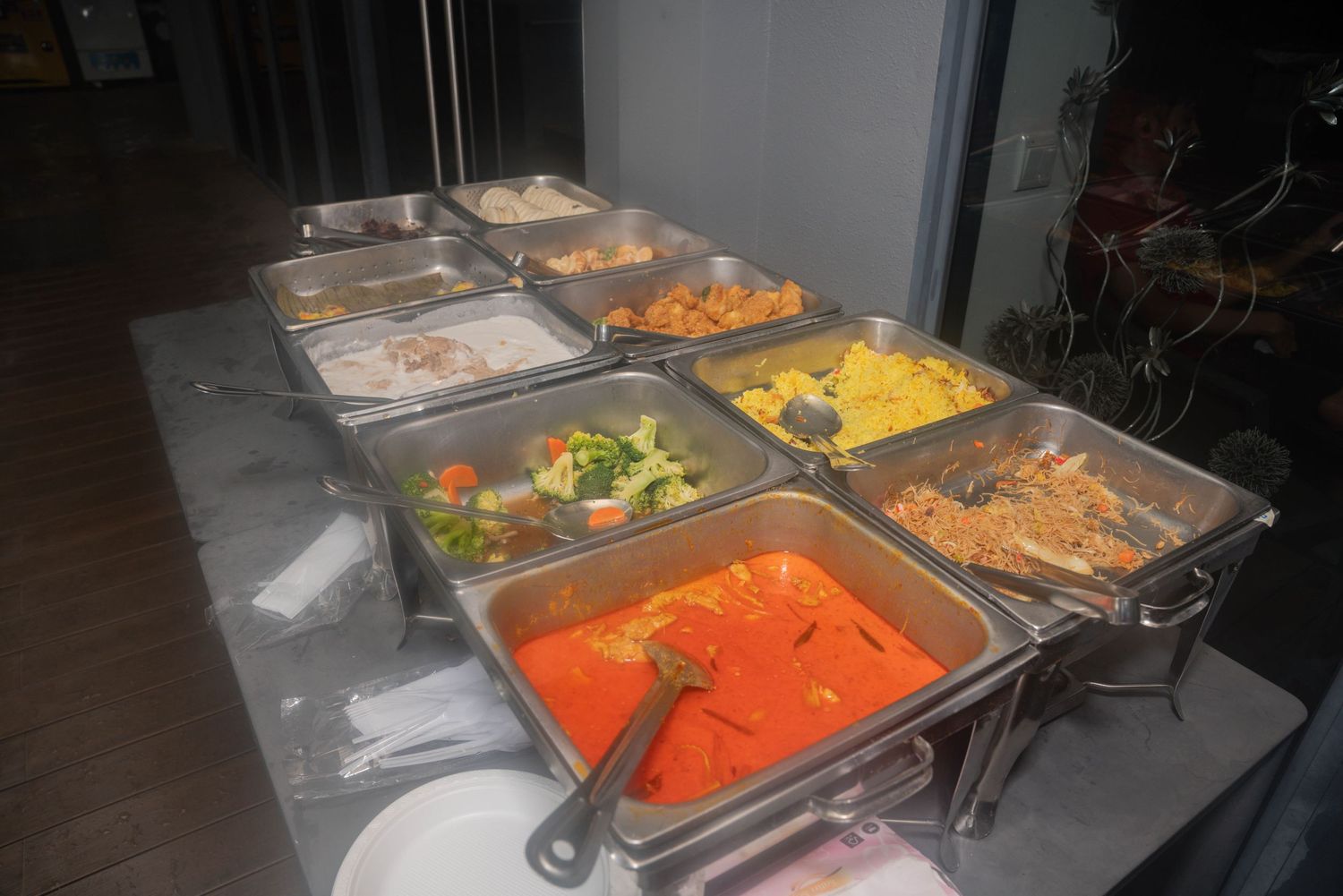 A buffet line with stainless steel serving trays filled with colorful foods in orange, yellow and green.