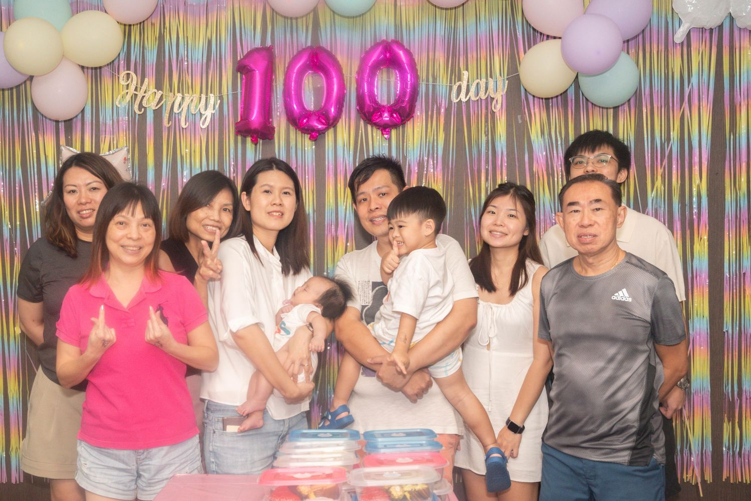 A festive 100 days celebration with colorful backdrop, pink balloon numbers, and party decorations.