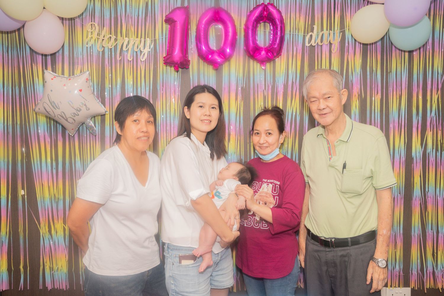 People celebrating a 100th birthday party with colorful decorations and festive balloons in the background.