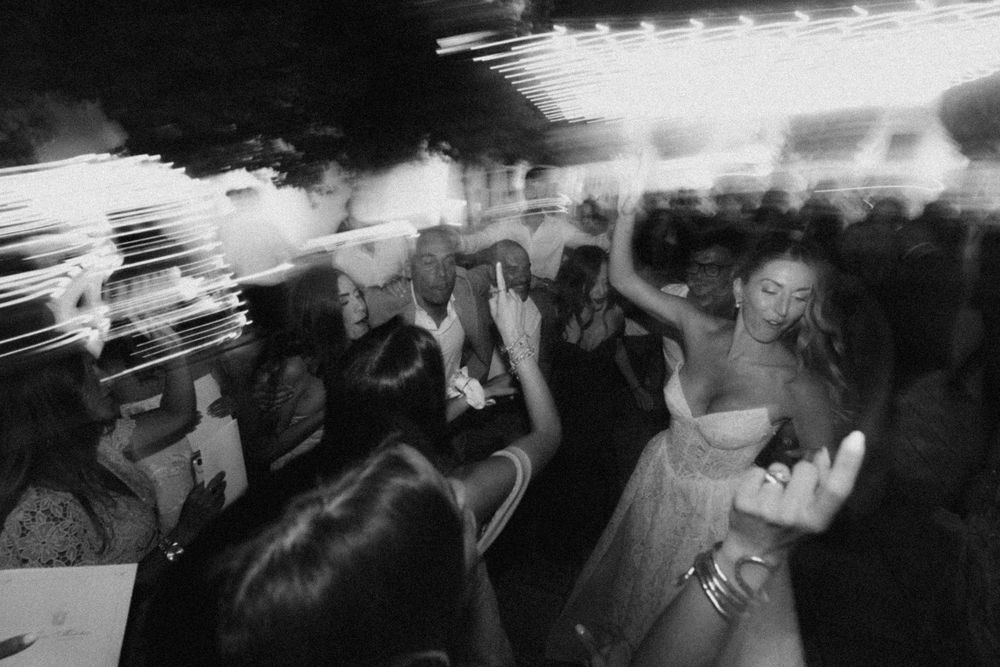 Black and white photo of people dancing and celebrating at a party with motion blur effects creating a dynamic atmosphere.
