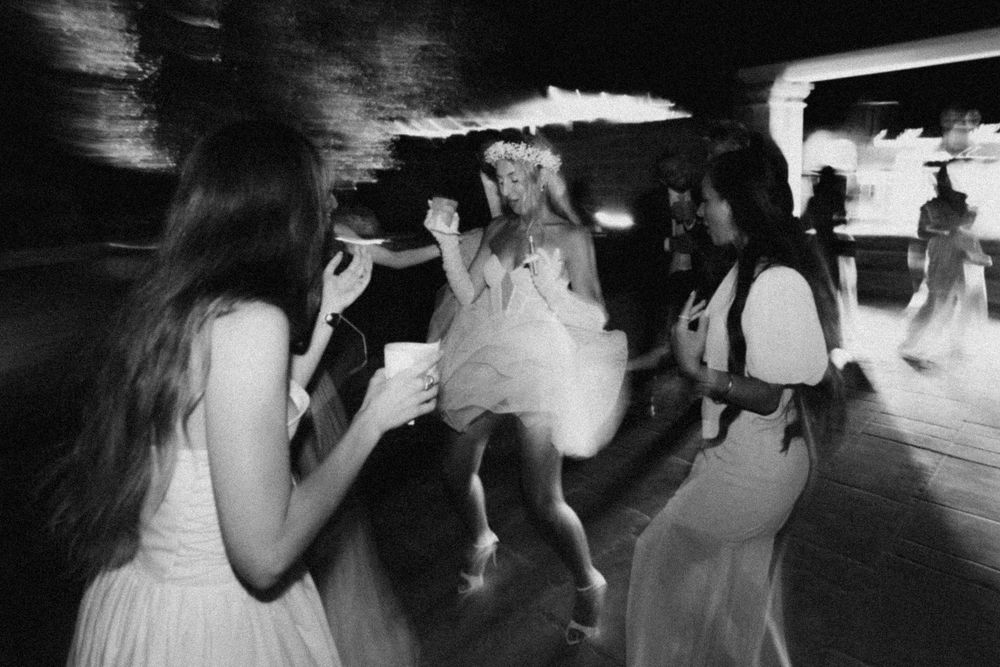 Black and white panoramic sequence showing wedding guests dancing and celebrating on a dimly lit dance floor.