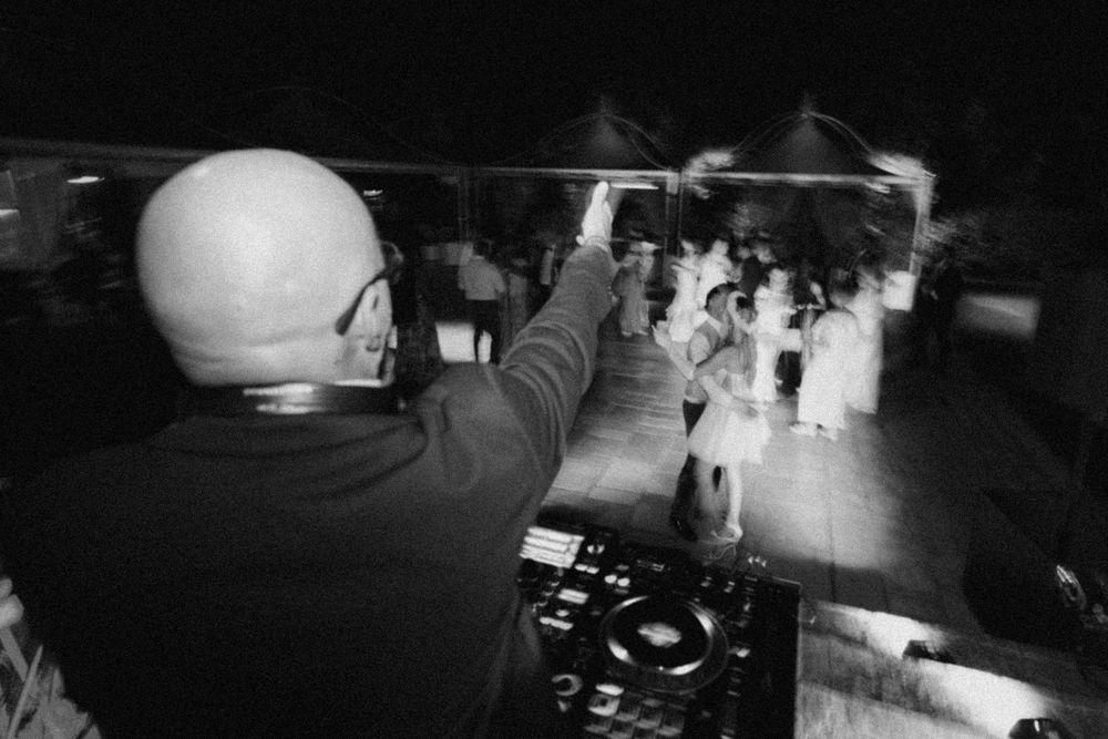 A DJ performs at a nightclub, viewed from behind while mixing music for the crowd on the dance floor.
