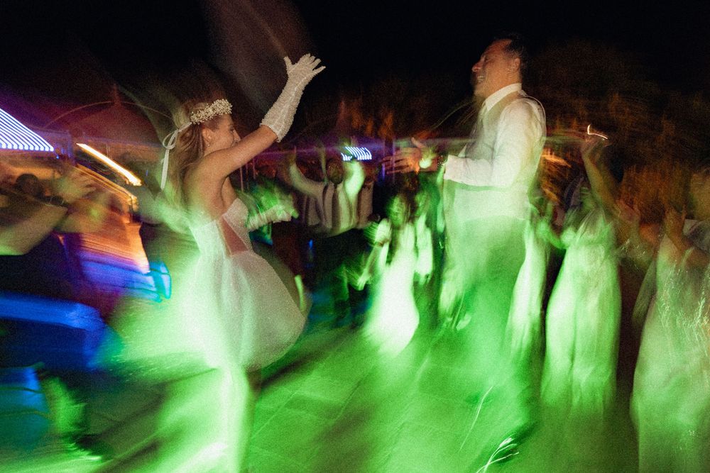 A motion-blurred dance floor scene at a wedding reception with green and blue lighting effects creating an ethereal atmosphere.