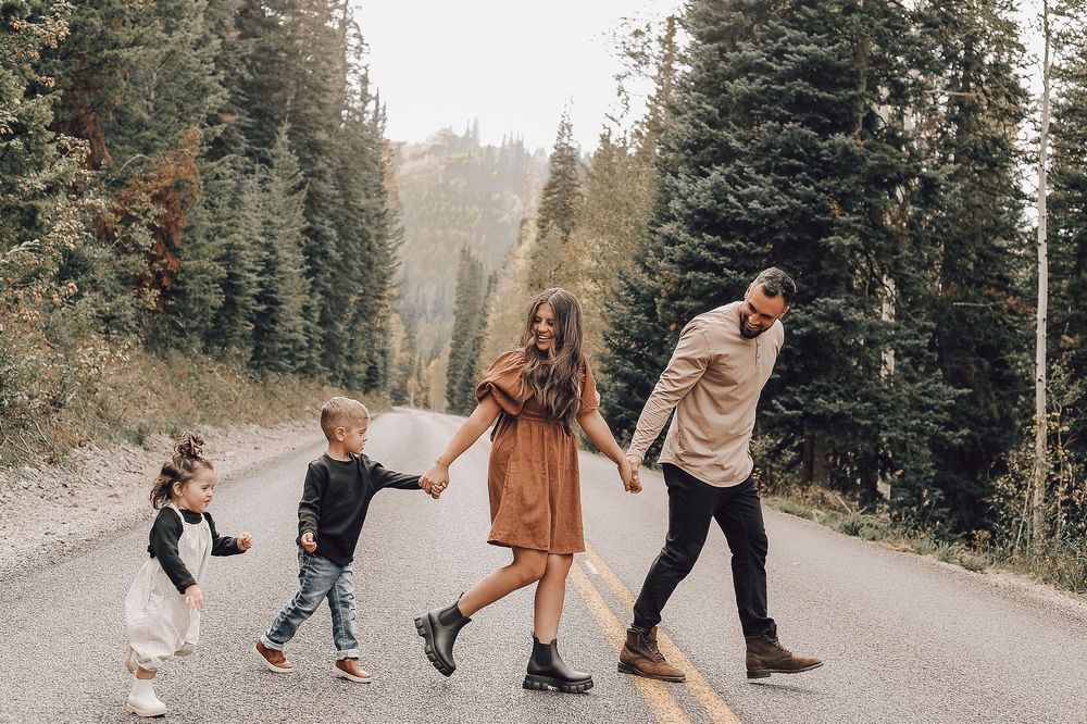 Family walking and playing together on a scenic mountain trail surrounded by evergreen trees.