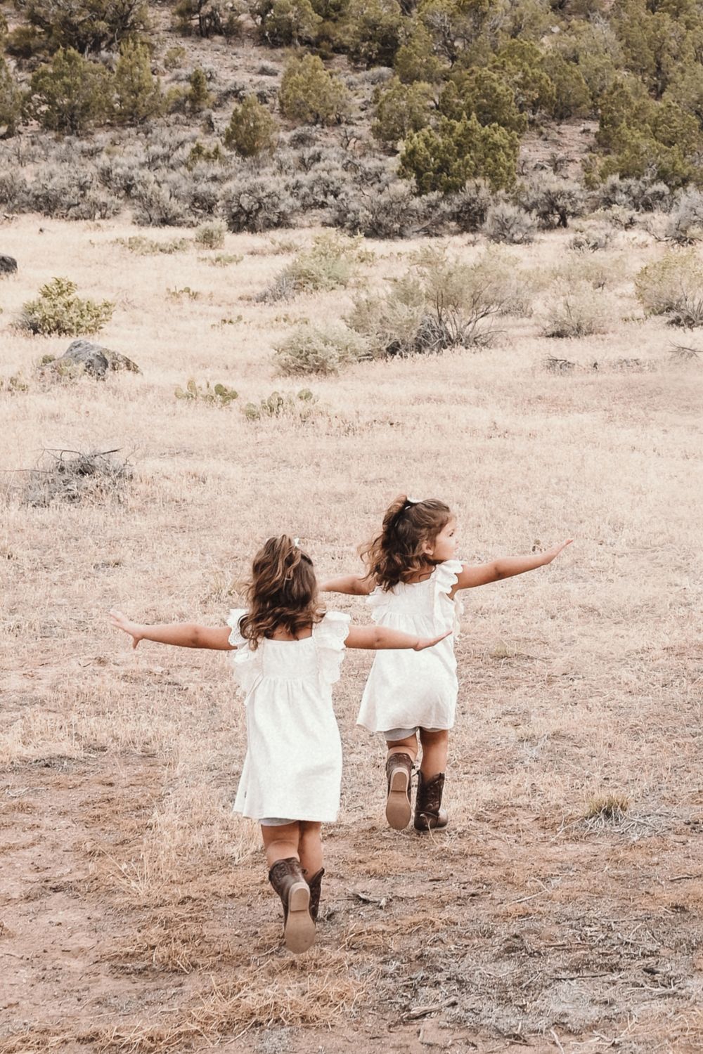 Four sequential photos show two small children in white dresses playing and posing together in a desert landscape.