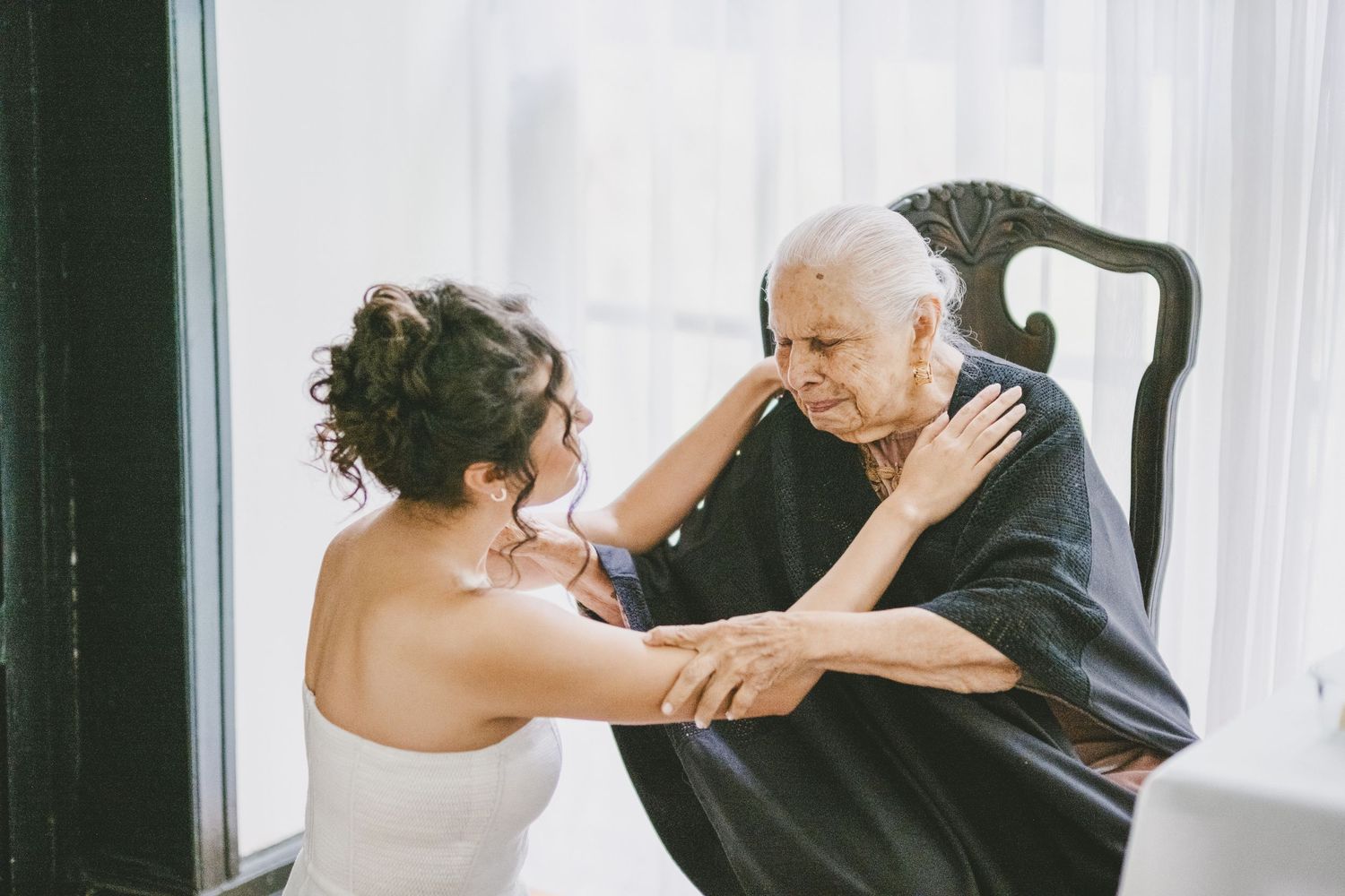 A tender moment of touching foreheads at a wedding, captured in front of a white curtained background.