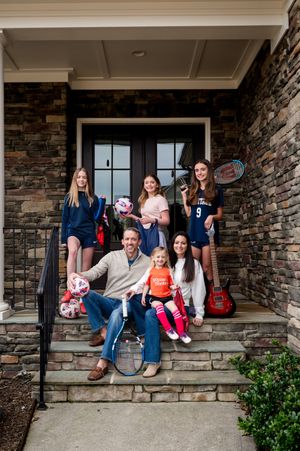 Family gathered on stone porch steps of a rustic house with stone walls.