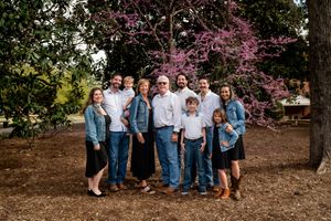Extended family group photo against blooming cherry trees in casual denim outfits.