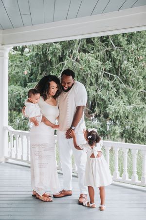 Family in coordinated white outfits sharing tender moments on a bright porch with white columns.