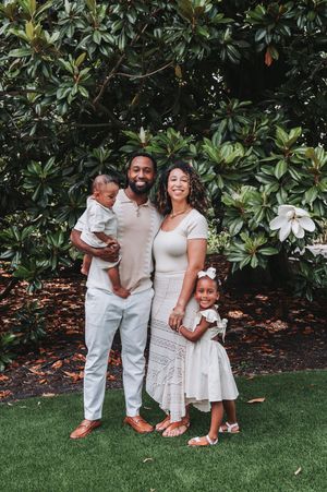 Family in coordinated white outfits poses against lush magnolia tree background.
