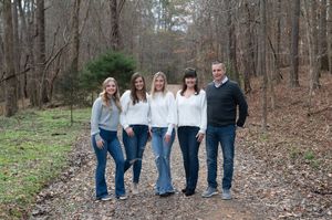 Family walking together through bare winter trees in matching denim and white outfits.