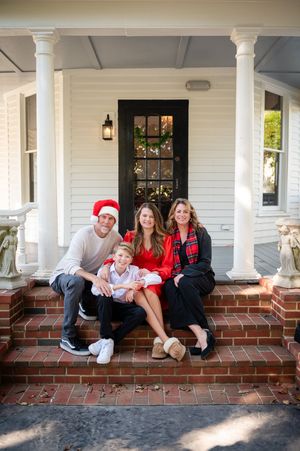 Family relaxing on brick steps of white colonial porch wearing casual winter clothing.