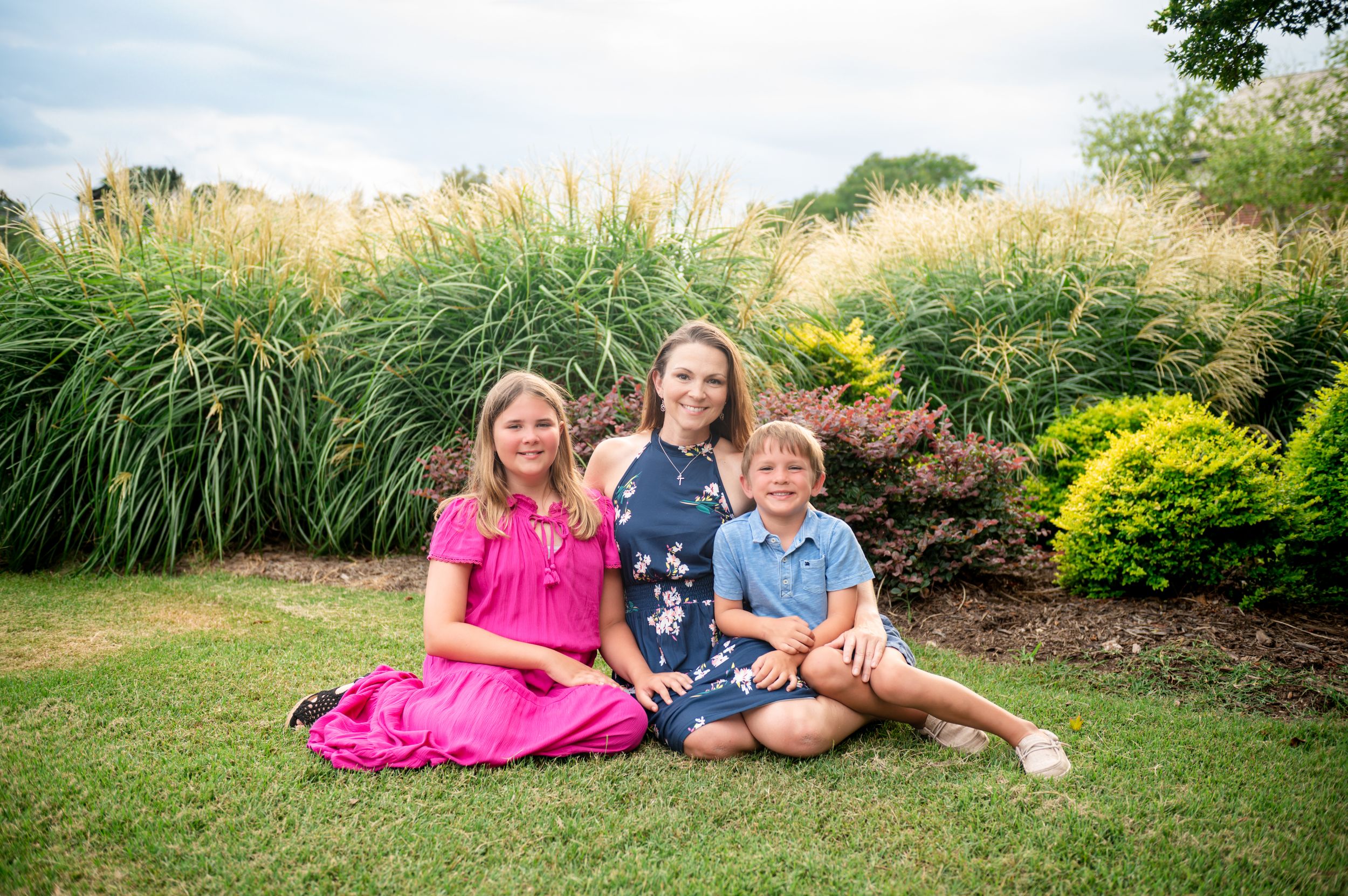 Family lying on grass together in casual attire during golden hour outdoor photo session.