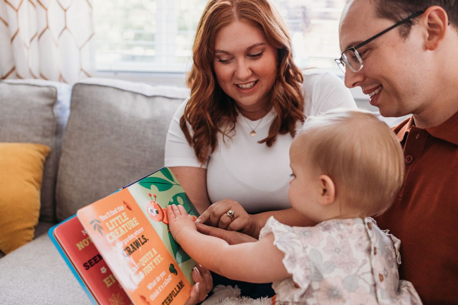 Parents and baby sitting on couch while reading storybooks together during family reading time at home.