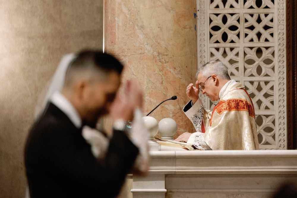 Priest performing wedding ceremony at ornate marble altar during Catholic church wedding.
