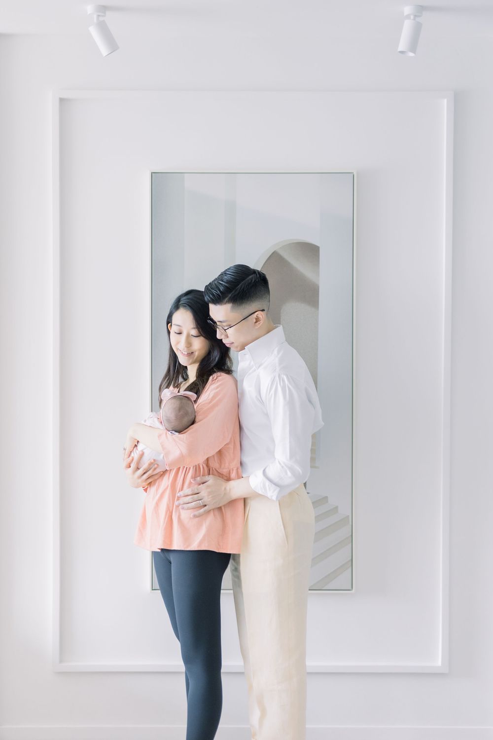 A couple embraces tenderly in a bright white studio setting wearing peach and white outfits for an engagement photoshoot.