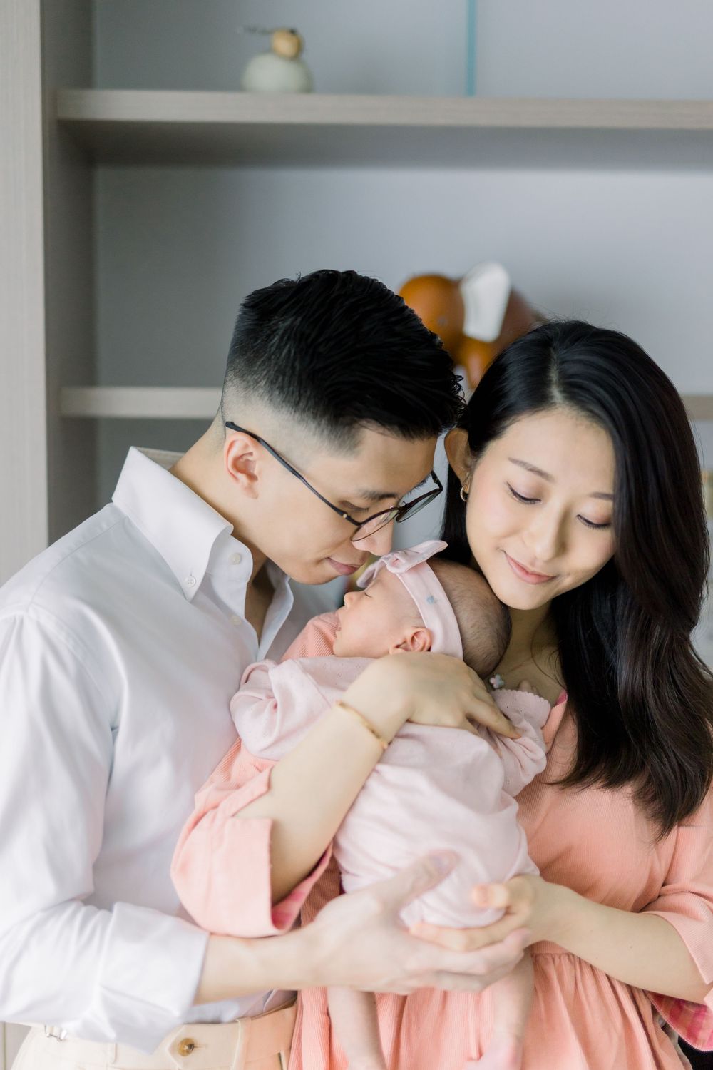 Parents in white shirts share tender moments with their baby wearing pink in a series of intimate family photos.