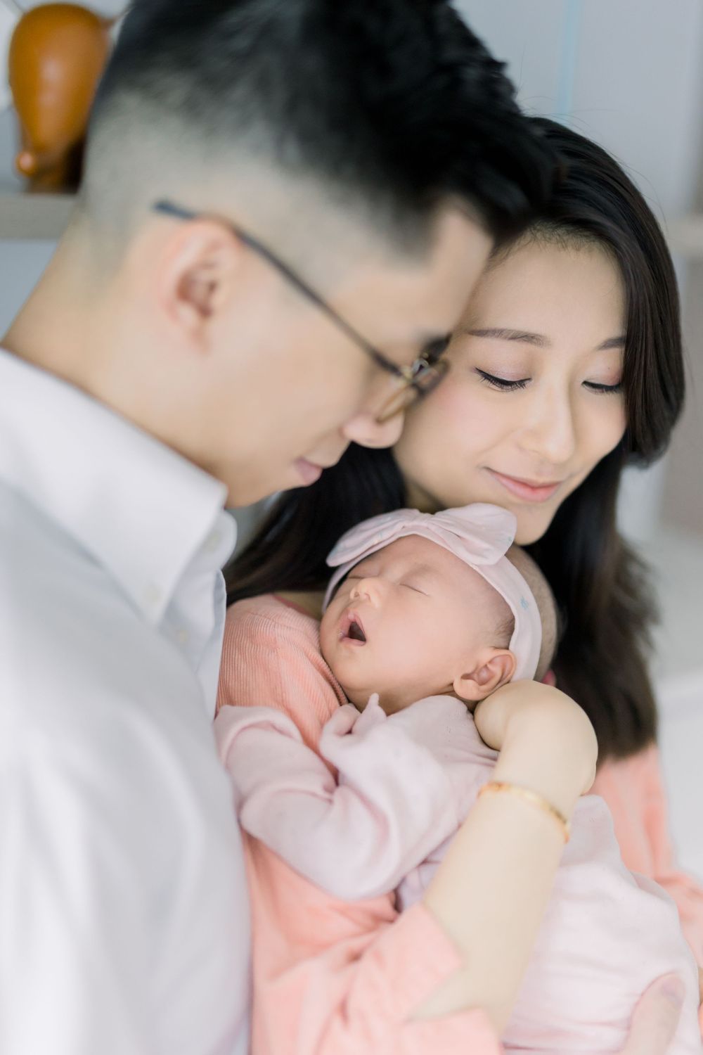 A tender family moment showing parents gazing lovingly at their sleeping newborn baby in soft lighting.