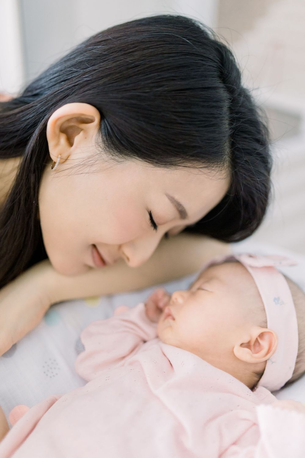 A tender moment between mother and sleeping baby in soft pink tones.