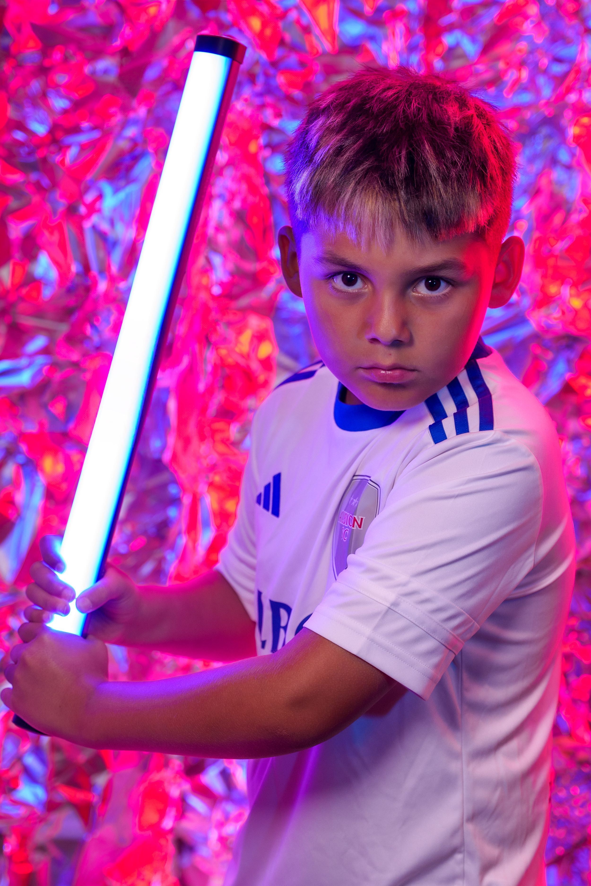 Action poses with glowing light saber against pink and blue backdrop while wearing white Albion uniform.
