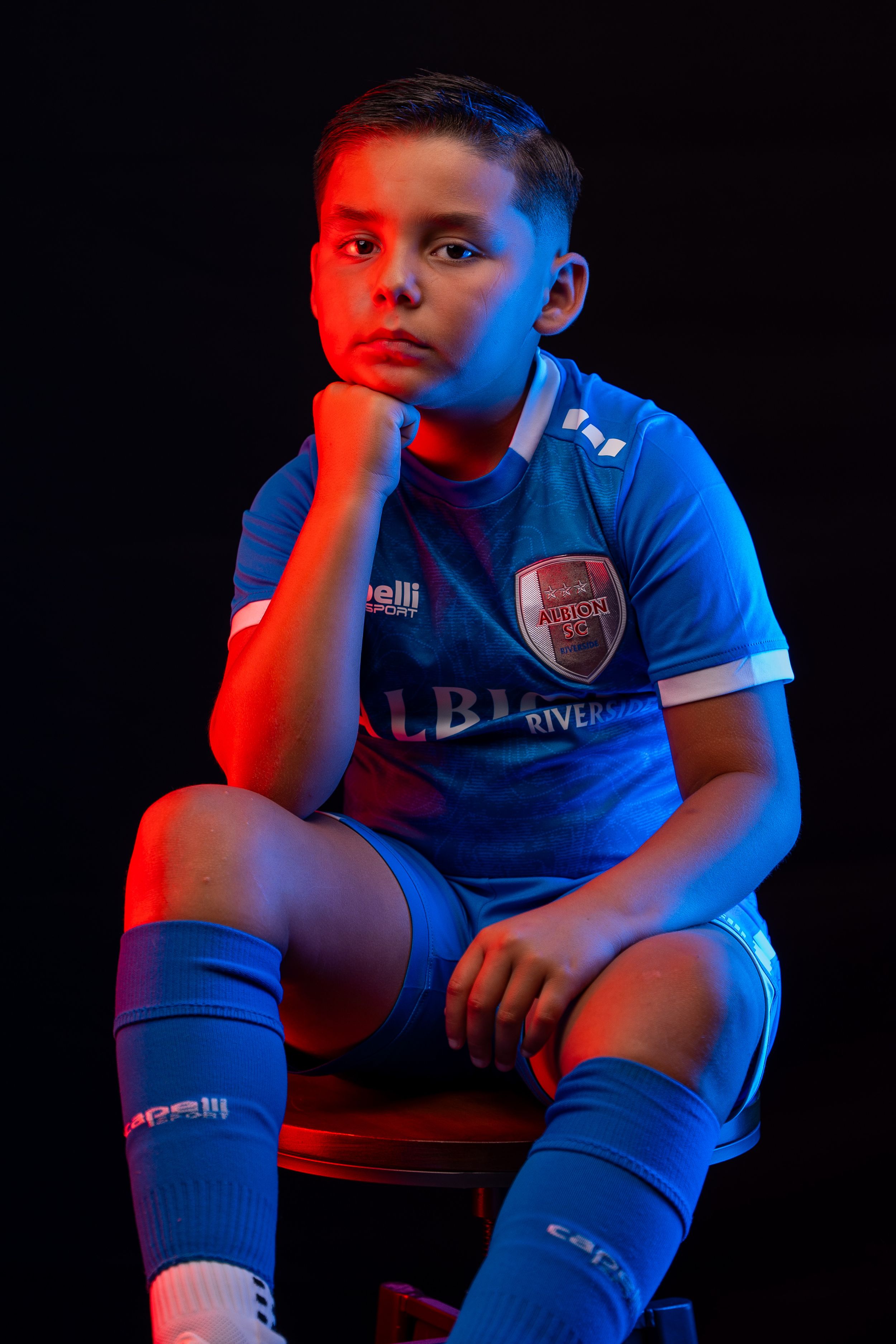 Soccer player posing in blue uniform against dark background with red lighting.