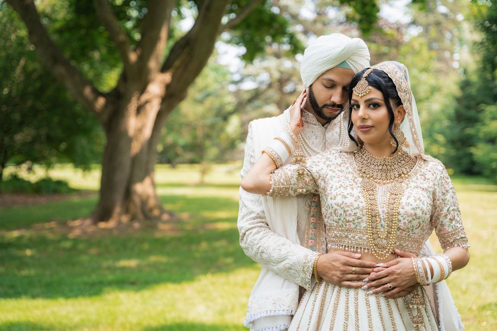 Wedding couple in matching cream and gold traditional attire embracing in a garden setting.