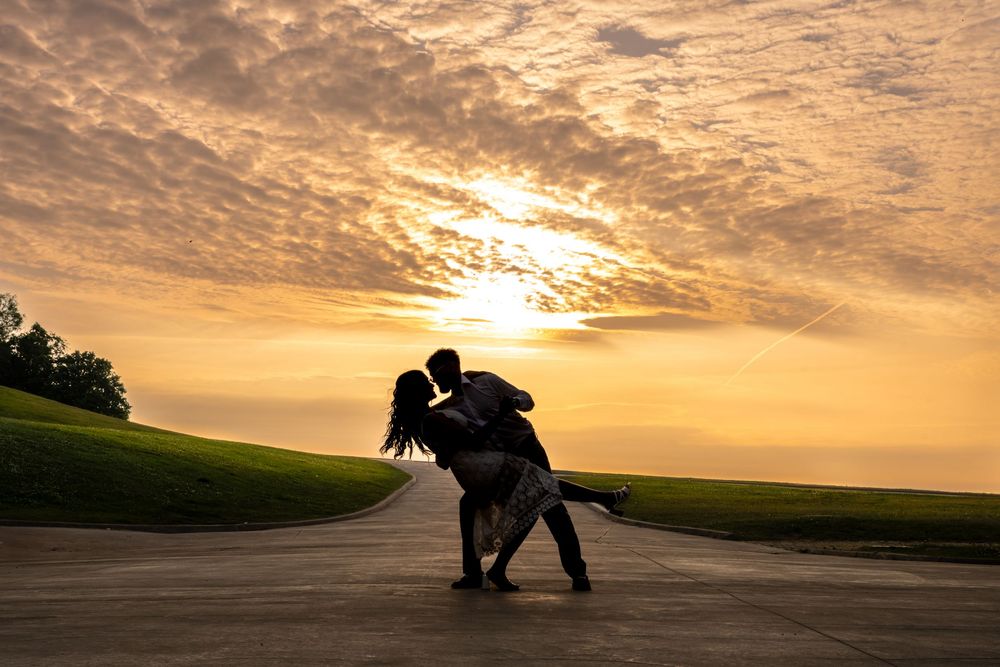 Silhouetted dancers perform a dramatic dip pose against a vibrant golden sunset sky.