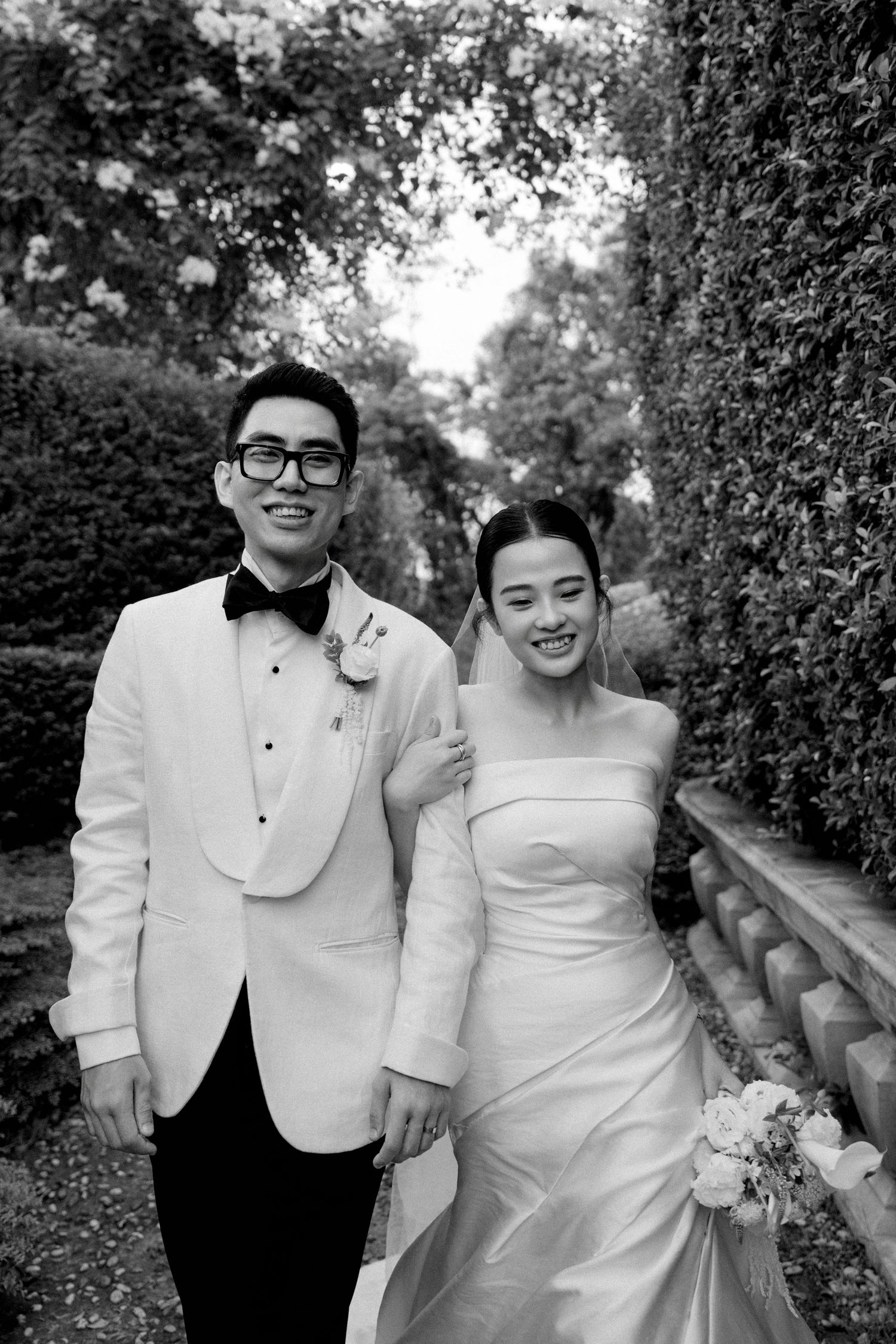 A playful black and white wedding photo sequence showing a couple laughing together in formal attire against a garden backdrop.