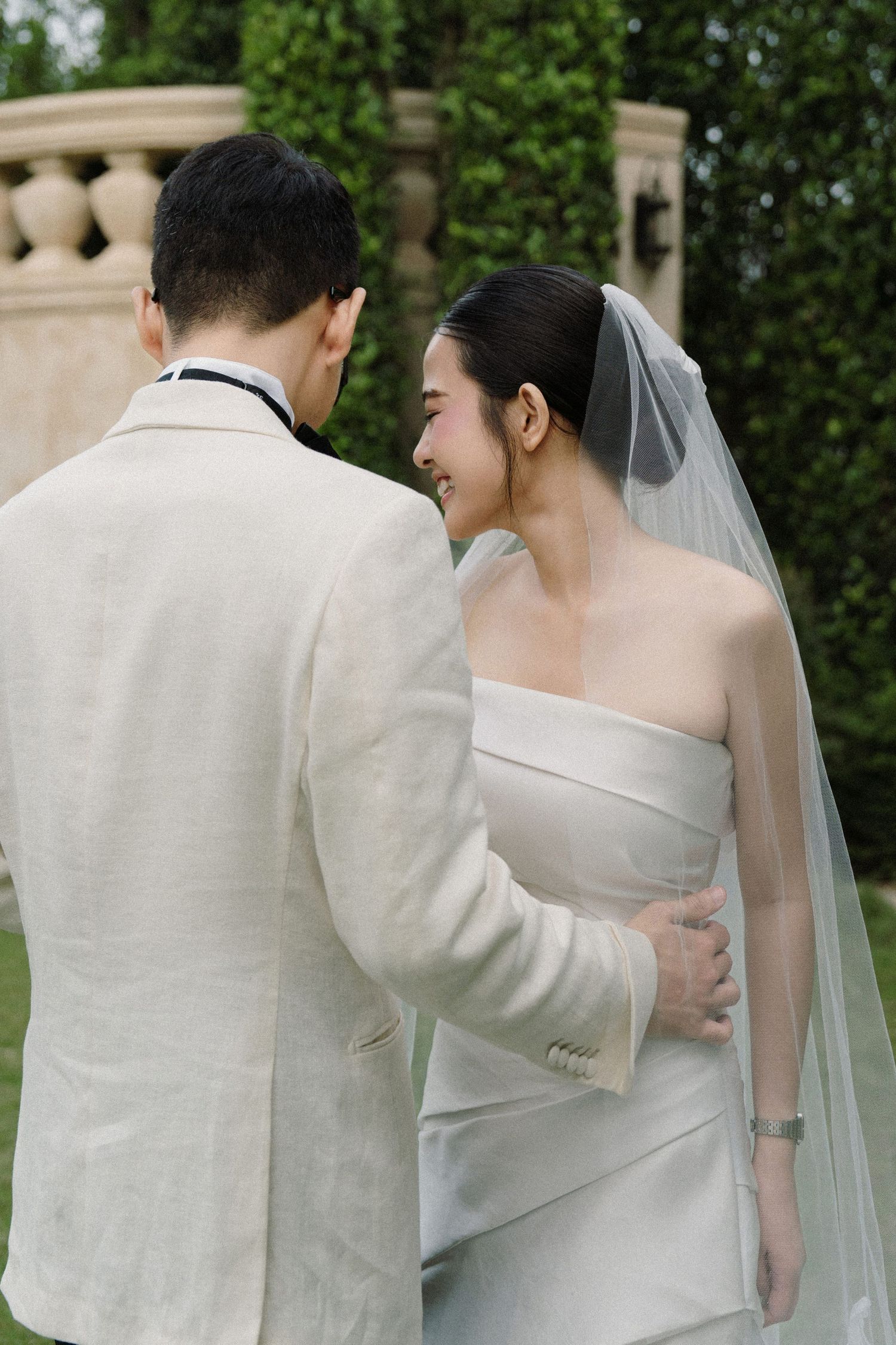 Elegant couple in wedding attire sharing a private moment against a lush garden setting.