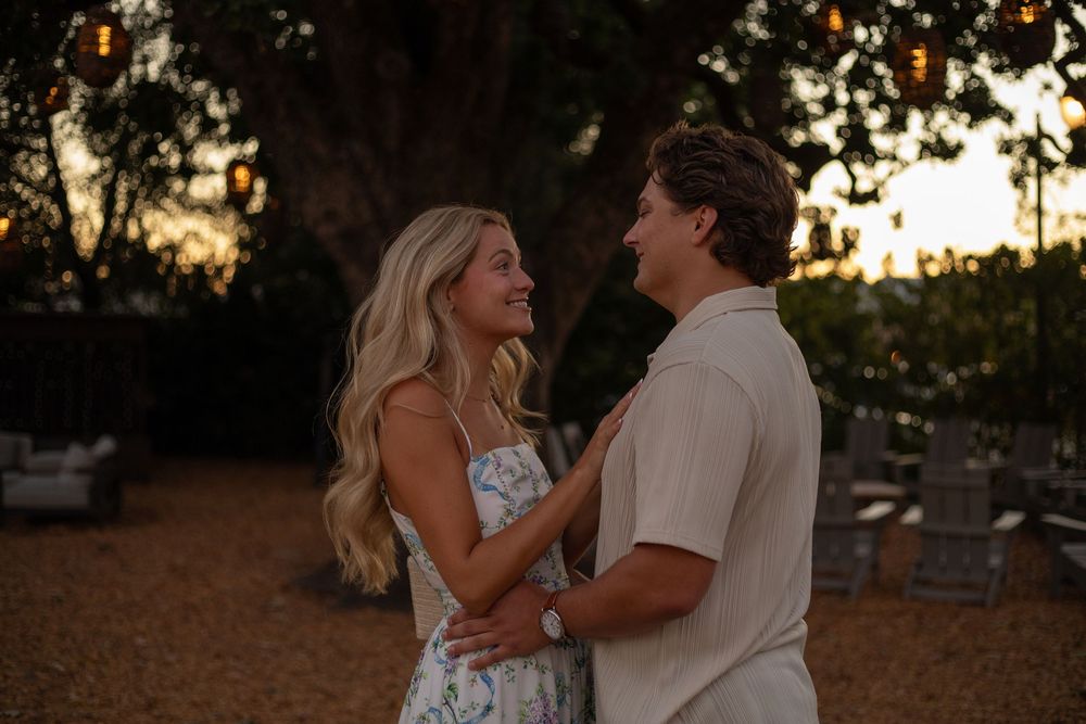 A tender proposal moment captured under a large tree with golden light filtering through.