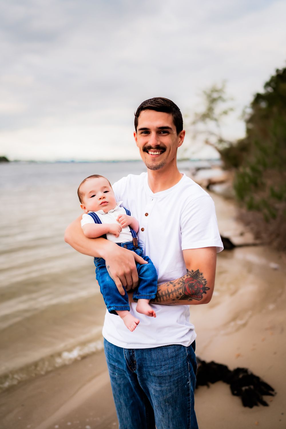 A series of beach portraits showing a person in a white t-shirt and jeans holding a baby on a sandy shore.