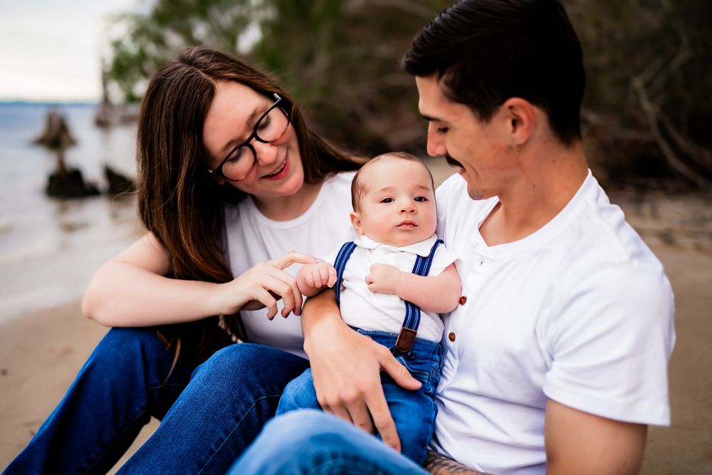 A baby in a blue shirt being held close outdoors during a family portrait session.