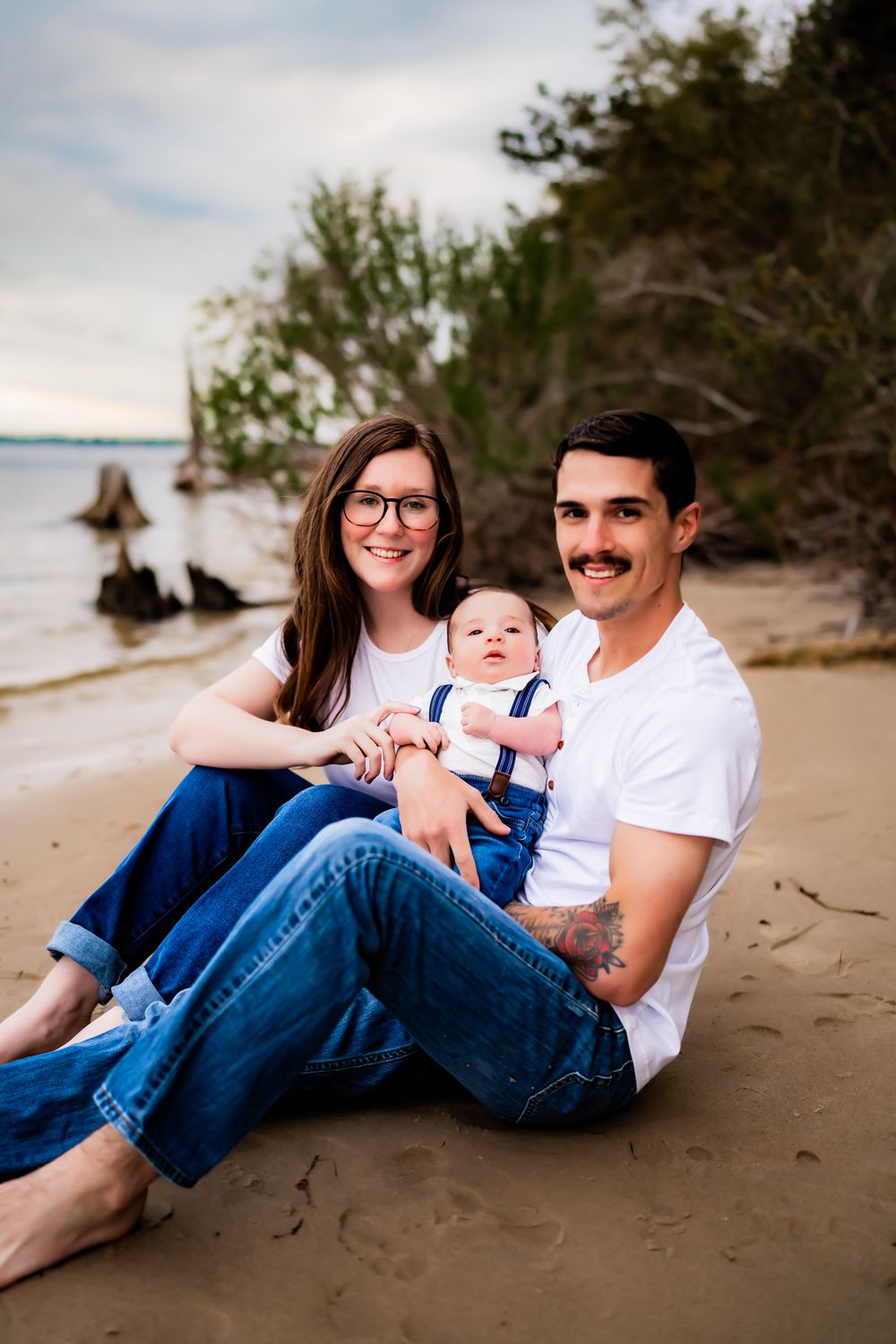 Family dressed in denim and white relaxing together on a sandy beach at sunset.
