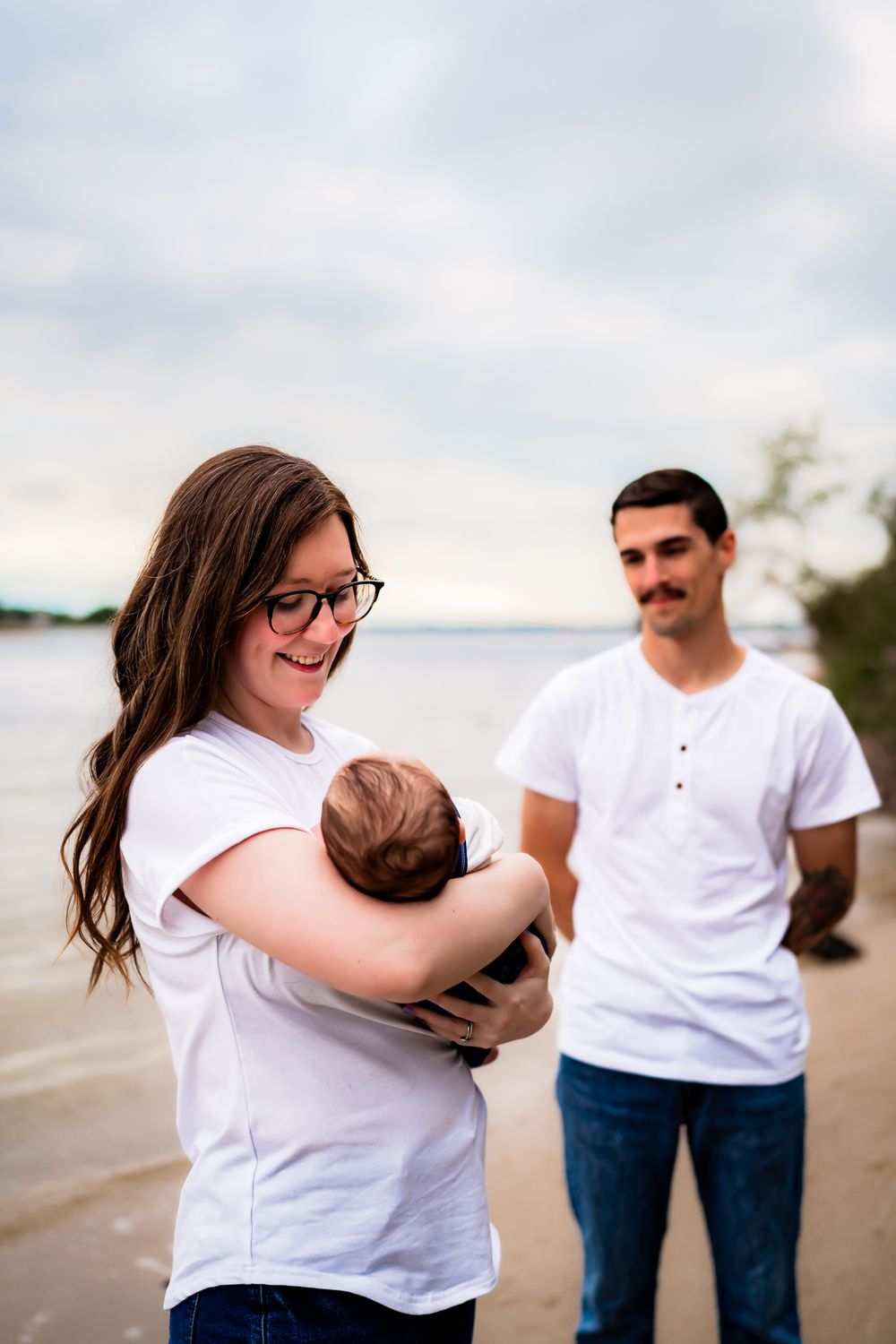 A family in casual white shirts enjoys tender moments together on a cloudy beach.